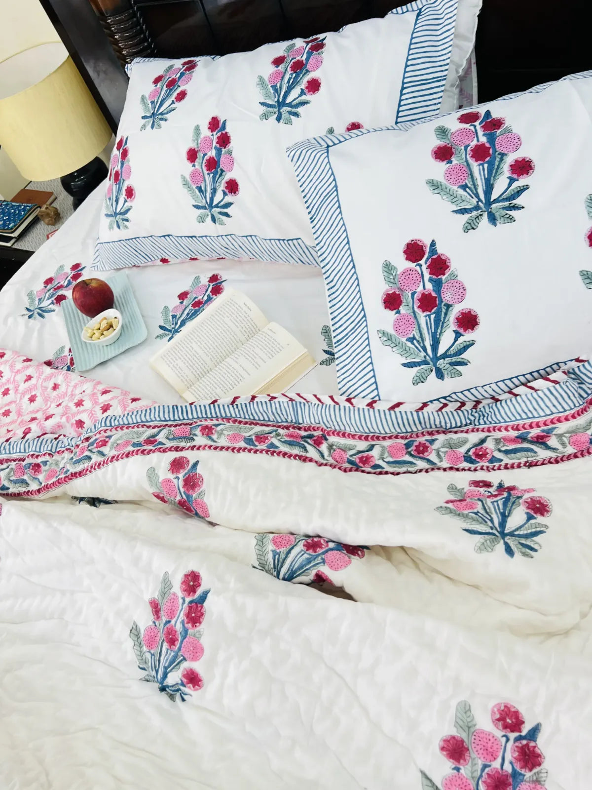 Floral embroidered bedding set on a bed with pillows and a blanket.