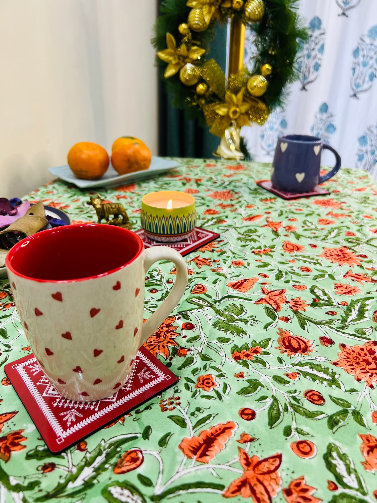 Decorative table setting with a floral tablecloth, red mug, and Christmas wreath.