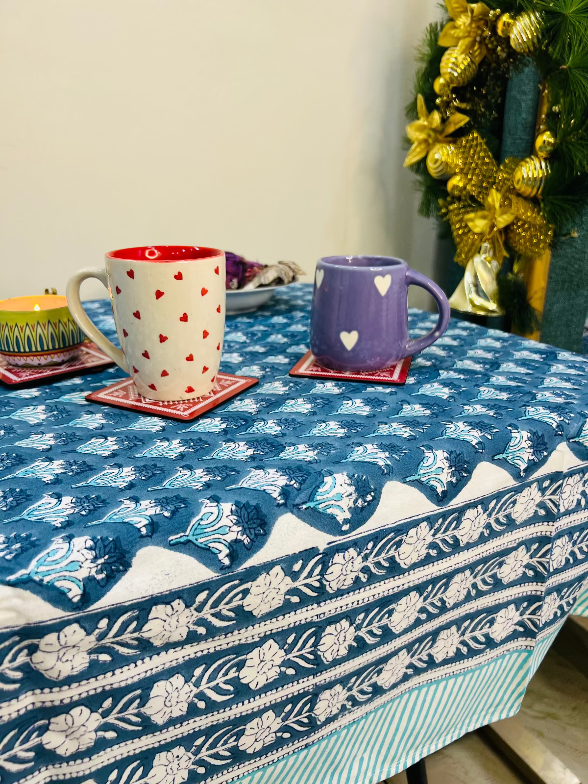 Table with blue floral tablecloth, two mugs, and a decorative wreath.