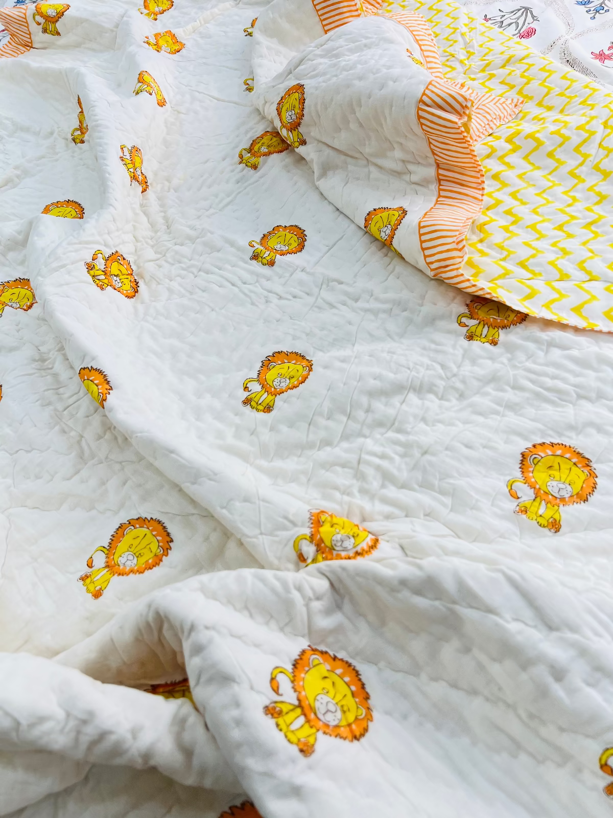 White fabric with orange lion prints and a folded yellow and white patterned item on top.