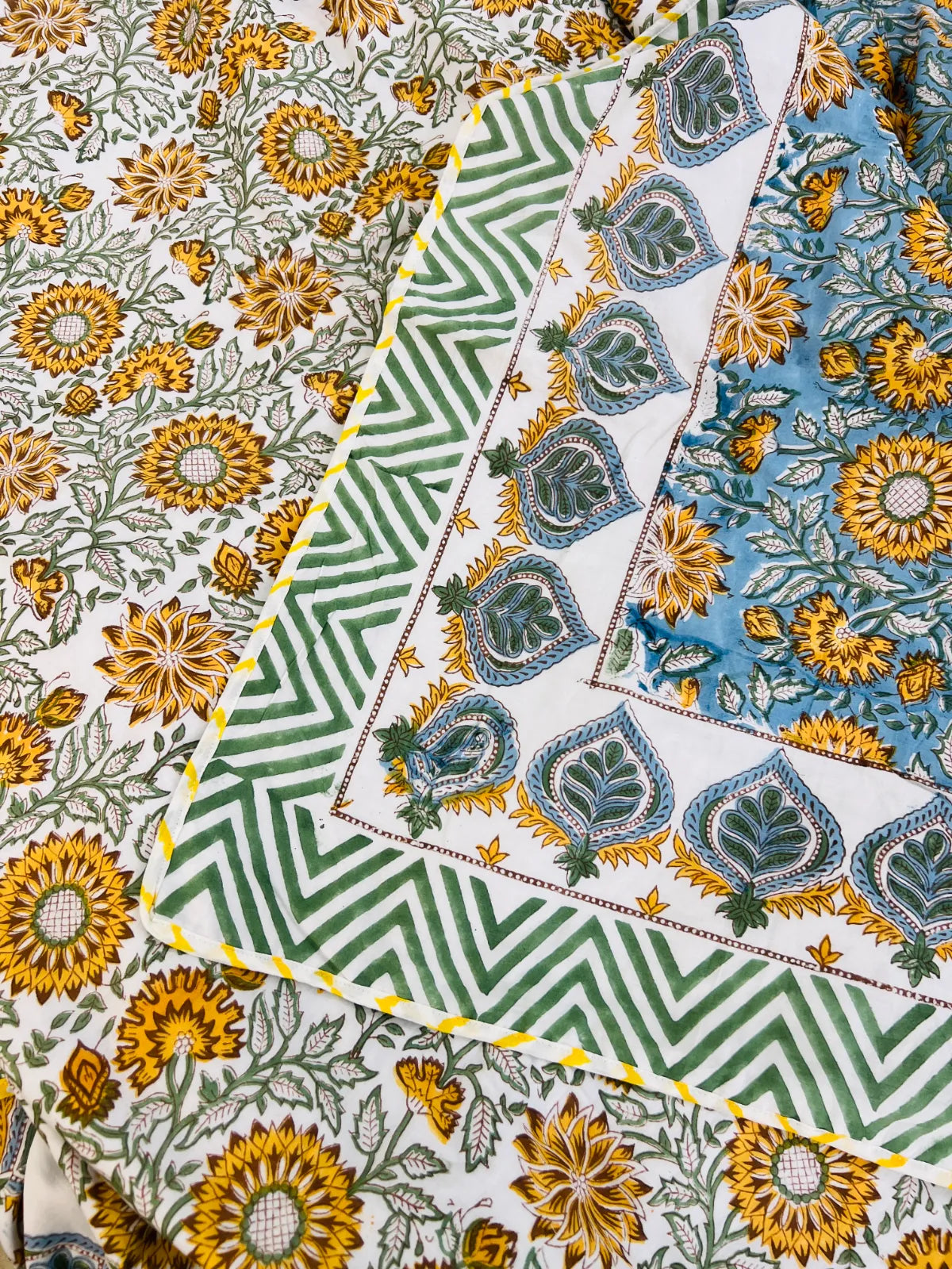 Three folded cotton fabric pieces with traditional block prints, featuring sunflower and floral motifs in yellow, blue, green, and white.