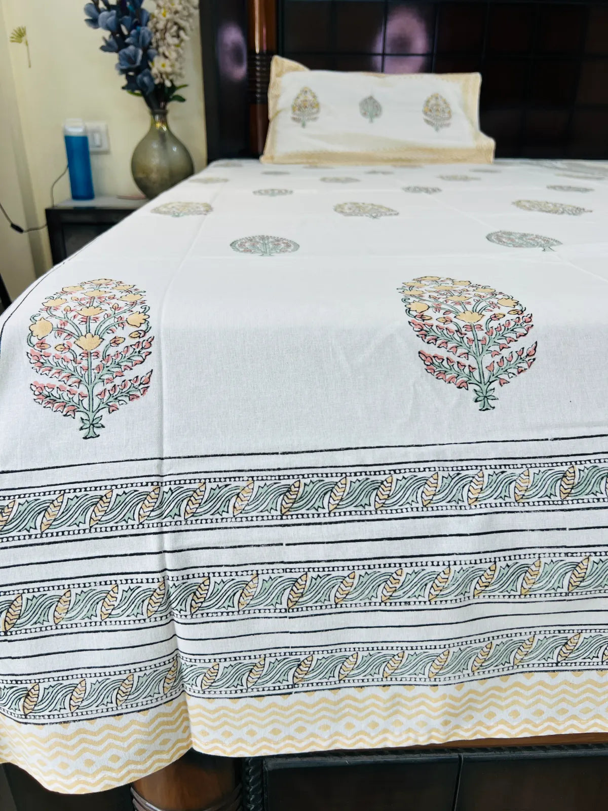 A white cotton bedspread with hand-block printed floral motifs and a decorative border, styled on a bed in a bedroom setting.