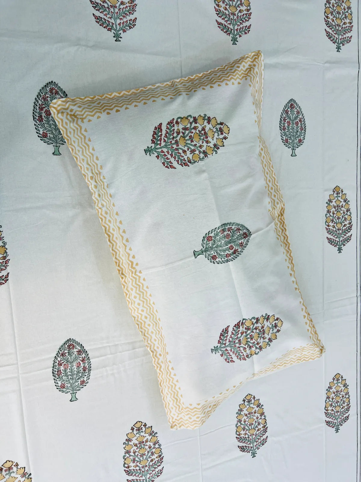 A white rectangular pillowcase with a beige scalloped border and colorful floral block prints, laid flat on a matching white printed sheet.