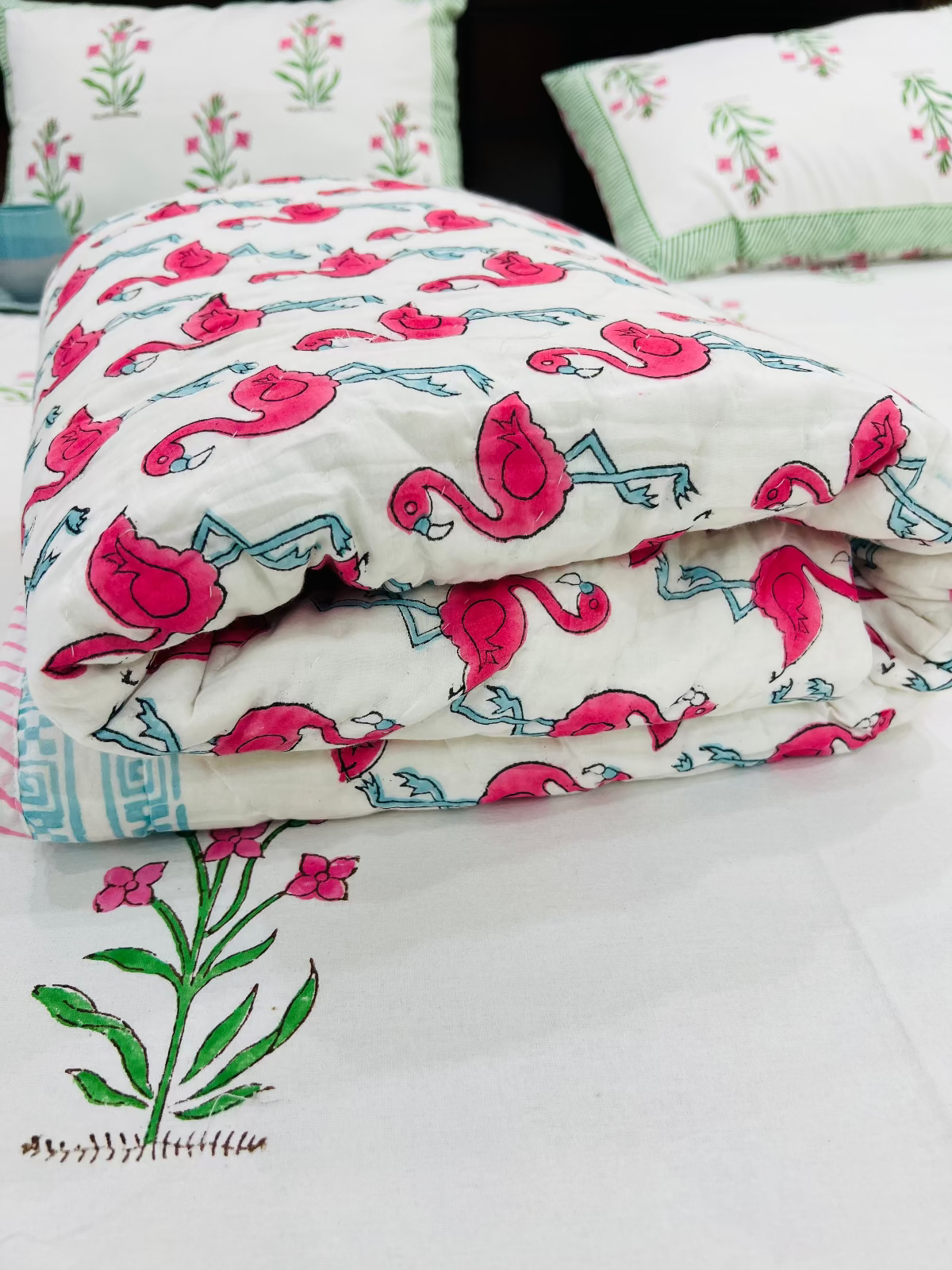 Floral and flamingo patterned bedding set on a bed with green floral embroidery.