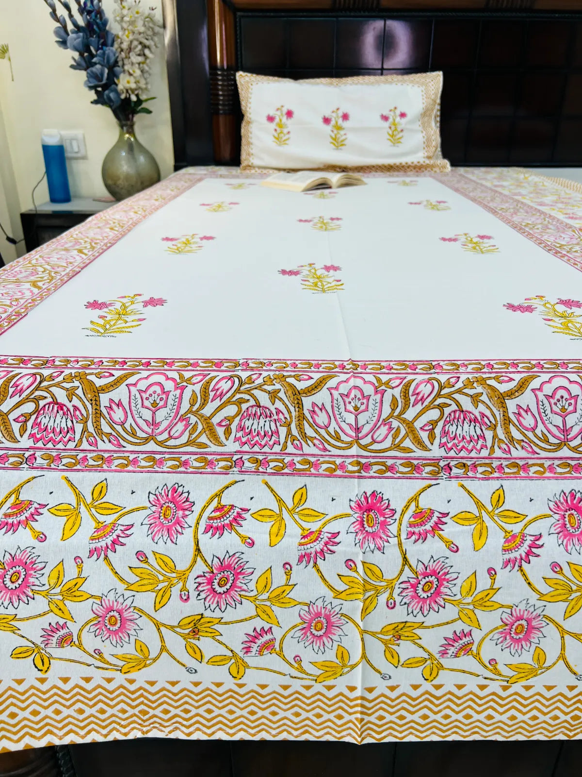 A white cotton bedspread or table runner with vibrant pink and yellow floral embroidery and a detailed border, displayed on a bed with a matching pillow.