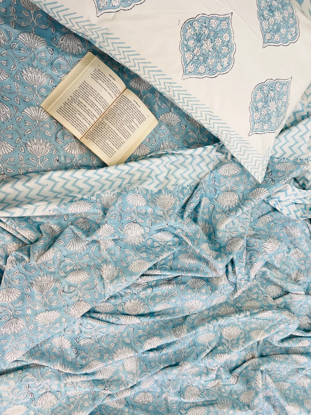 Light blue and white patterned bedding set with a matching pillowcase and an open book styled on top.